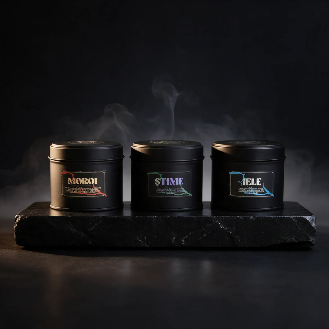 Trei lumânări parfumate de lux în recipiente negre pe o bază de piatră, cu fum fin de parfum.