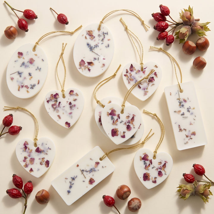 Handmade white wax sachets with dried flowers in heart, oval, and rectangular shapes.